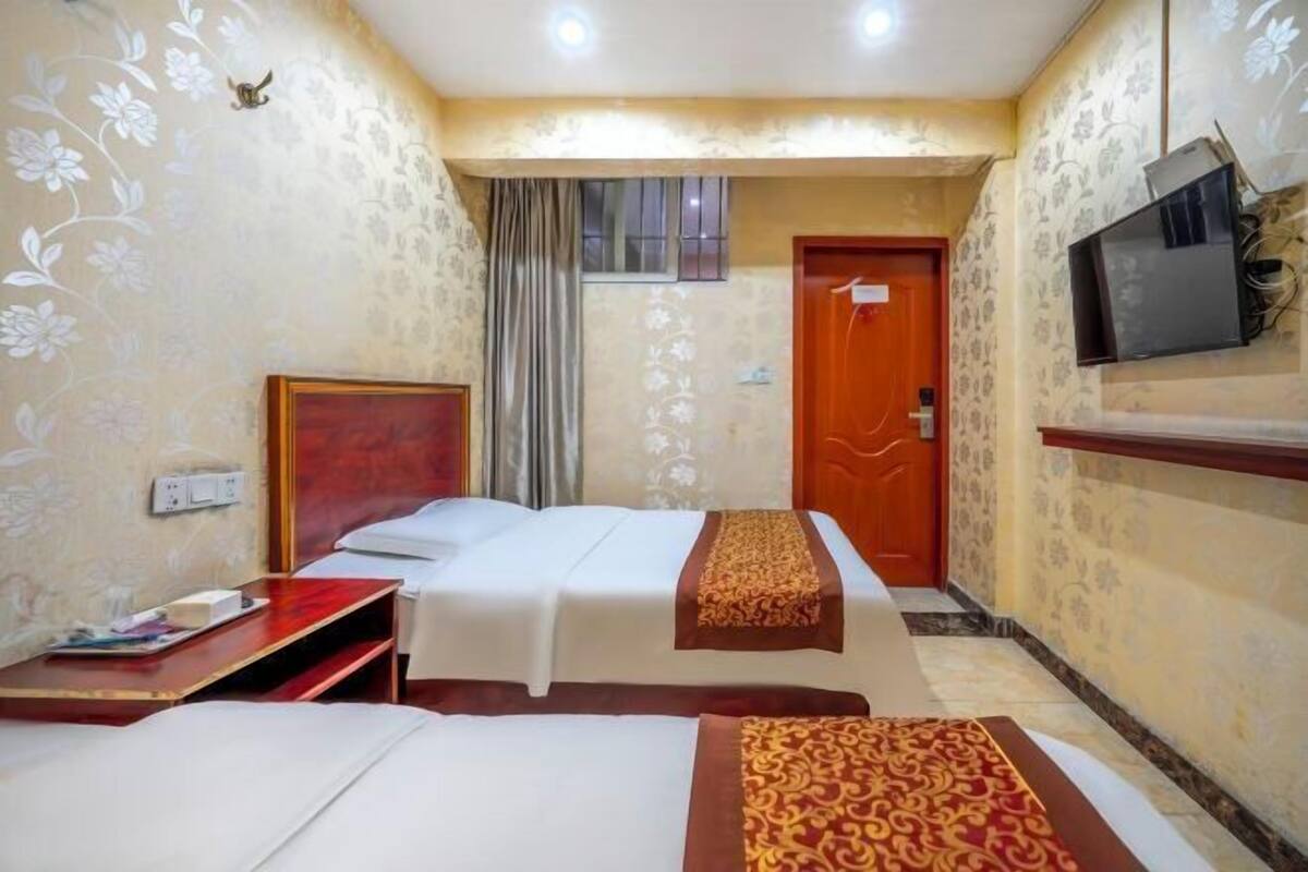 A hotel room with two beds, a TV mounted on the wall, a wooden door, and a window with curtains.