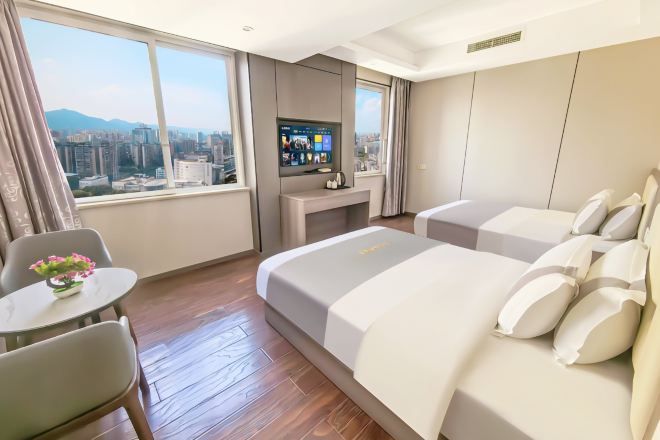 Ett hotellrum med en säng, en TV, ett skrivbord och utsikt över staden.