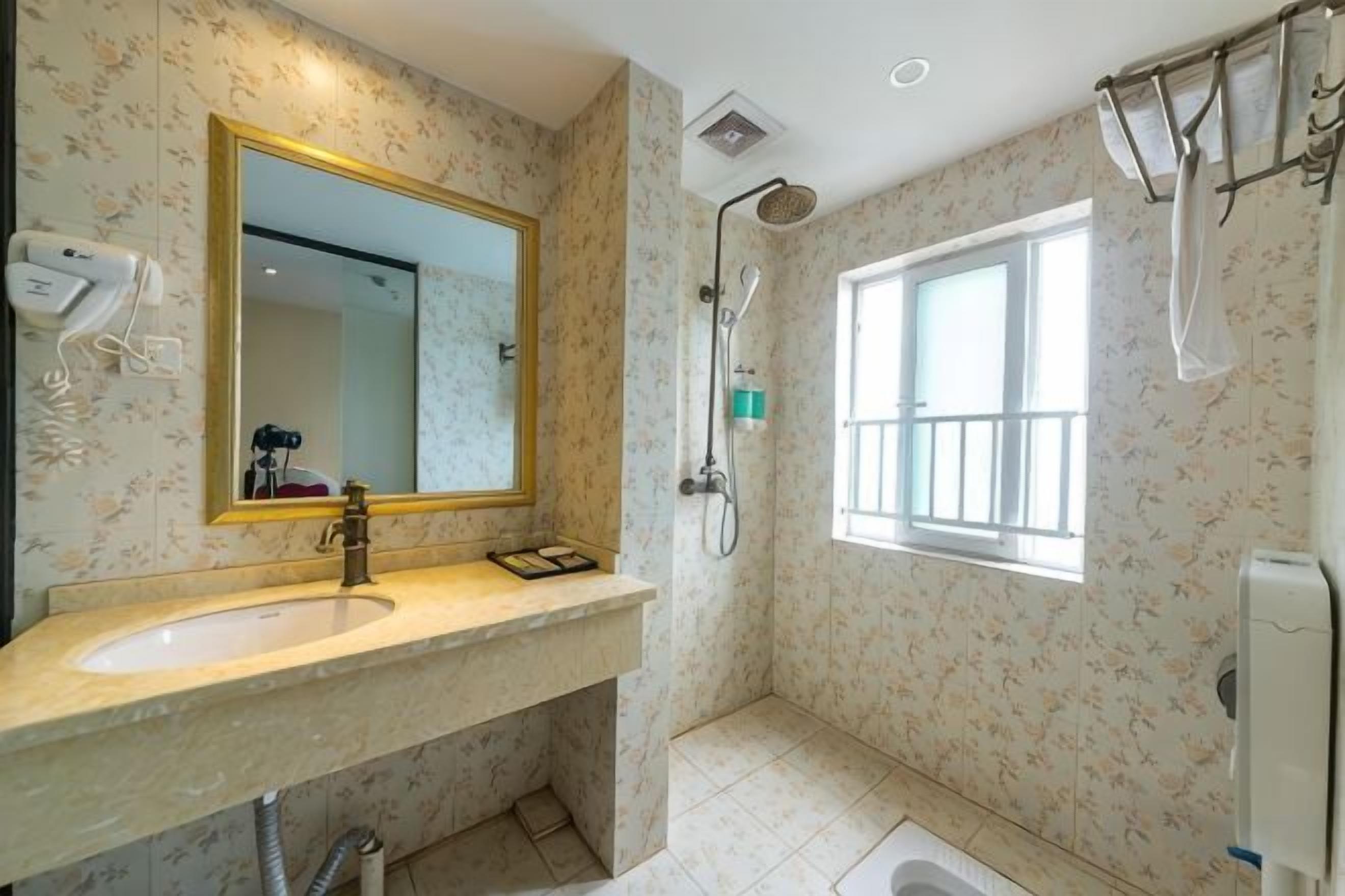 A bathroom with a sink, mirror, shower, and window.