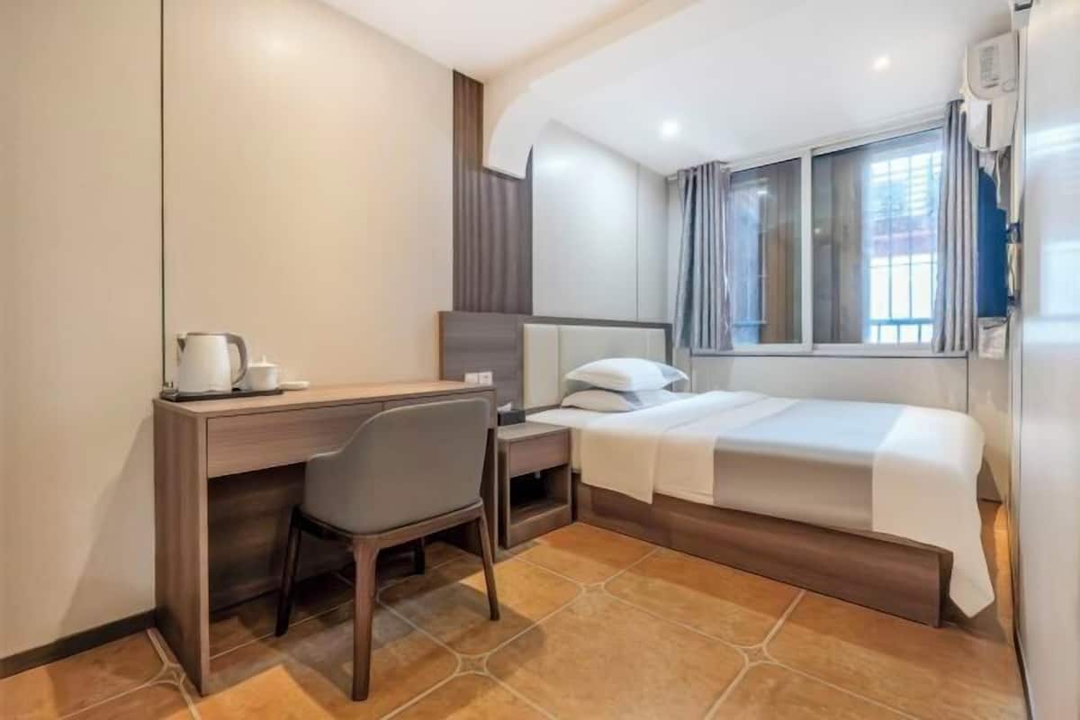 A compact hotel room with a bed, a desk, a chair, a nightstand, and a window.