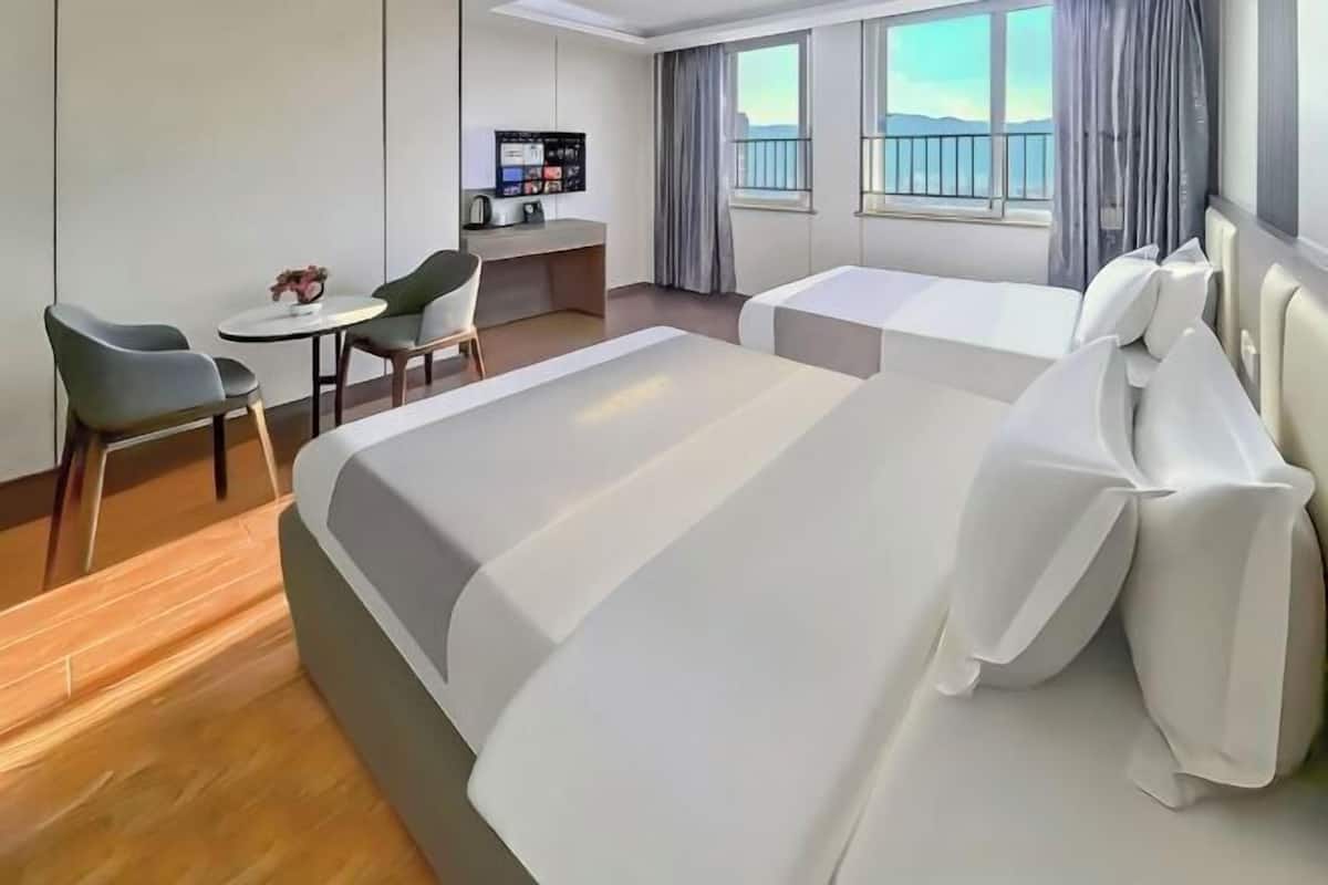 A hotel room with a large bed, a desk, a chair, and a small table. There is a window with curtains and a view of the outside.