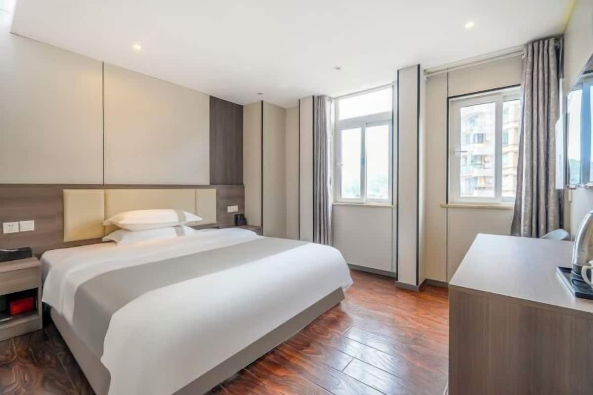 A modern hotel room with a large bed, a desk, and a window with curtains.