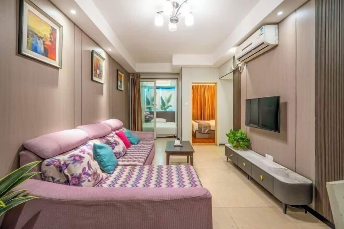 A modern living room with a sofa, TV, and a sliding door leading to a bedroom.