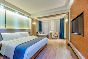 A hotel room with a large bed, a TV, a desk, and a chair.