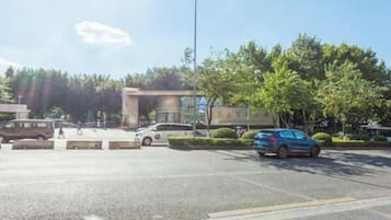 Un parking avec des véhicules, l’entrée d’un bâtiment et des arbres.