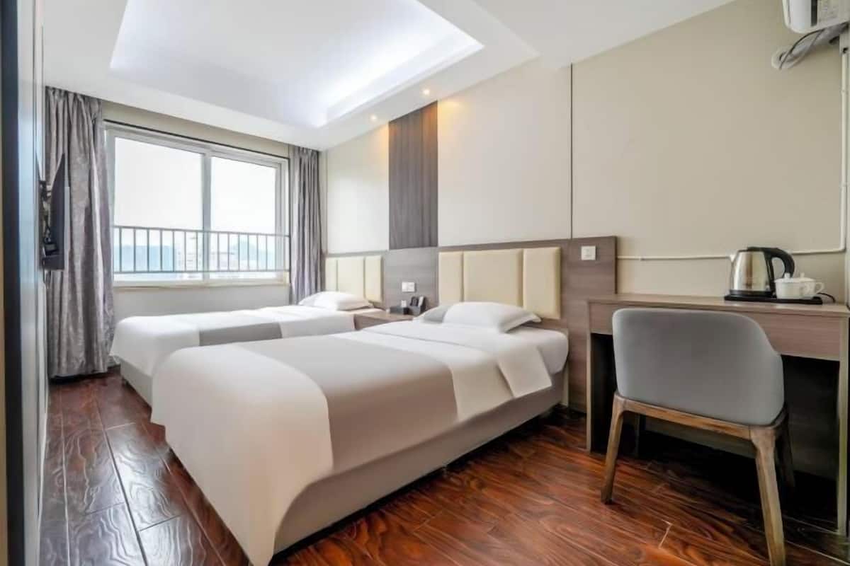 A hotel room with two beds, a desk, a chair, and a window with curtains.