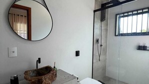 A modern bathroom with a stone sink, a white toilet, a glass shower enclosure, and a large mirror.