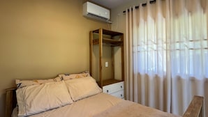 A bedroom with a bed, a wooden wardrobe, a mirror, and an air conditioning unit.