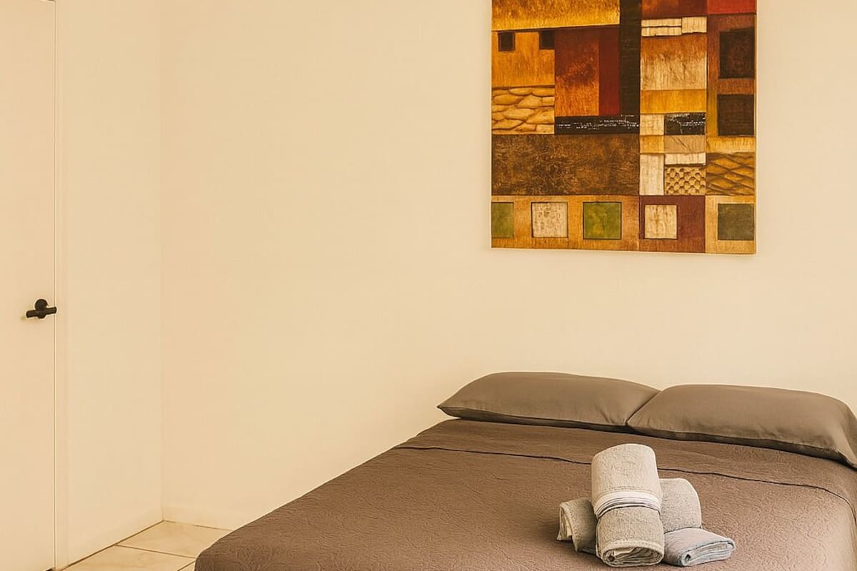 A neatly made bed with a brown bedspread and pillows, a wall art piece above it, and a door to the left.