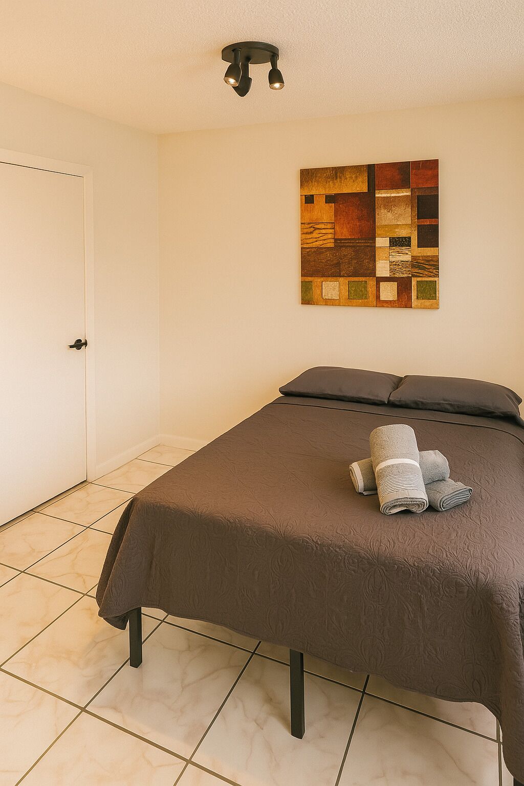 A neatly made bed with a brown cover, a wall-mounted artwork, and a door to the left.