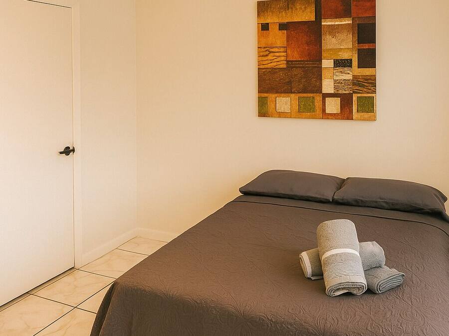 A neatly made bed with a brown cover, a wall-mounted artwork, and a door to the left.