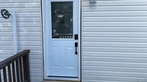 Una puerta blanca con un panel de vidrio, un buzón y un accesorio de luz en una casa con revestimiento horizontal.