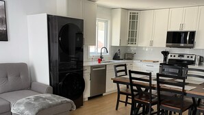 Una cocina moderna con armarios blancos, un comedor con mesa y sillas de madera, y un sofá gris.