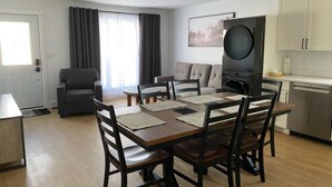 Una sala de estar moderna con un sofá, una mesa de comedor con sillas, una zona de cocina con armarios y un televisor de pantalla plana grande.
