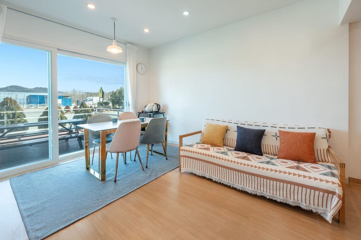 A modern living room with a sofa, chairs, a dining table, and a large window offering a view of a construction site.