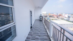 A narrow balcony with a tiled floor and a railing, overlooking a cityscape with buildings and a golden structure. - Bona Hostel PP (Phnom Penh)