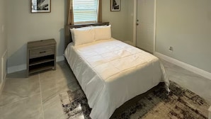 Une chambre à coucher avec un lit, une table de chevet, un ventilateur de plafond et une porte.