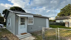 Une petite maison à un seul étage, à l’extérieur blanc, avec une porte d’entrée et un petit porche.