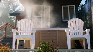 A house with a covered porch, two white Adirondack chairs, and a small table.