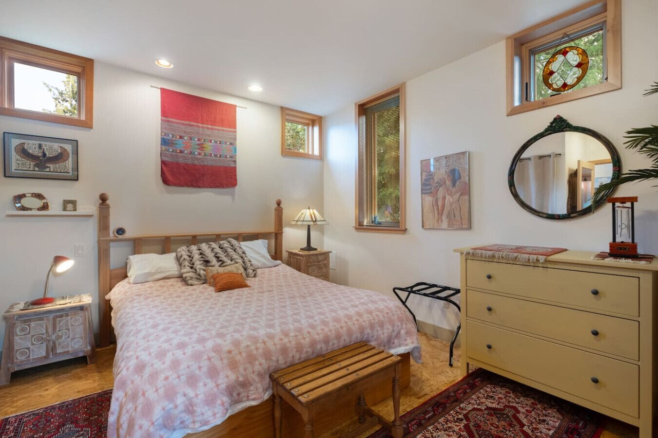 A bedroom with a bed, bedside tables, a dresser, a mirror, and artwork on the walls.