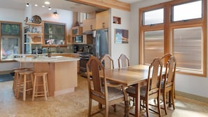 A modern kitchen with wooden cabinets, a central island with stools, and a dining table with chairs. - Custom Charm! Central - Office & Peaceful yard! (Seattle)