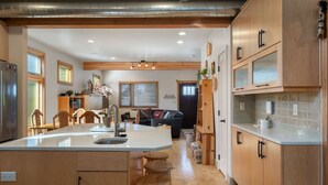 A modern kitchen with wooden cabinets, a central island with stools, and a dining area with chairs and a sofa. - Custom Charm! Central - Office & Peaceful yard! (Seattle)