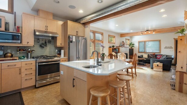 A modern kitchen with stainless steel appliances, wooden cabinets, and a central island with stools. - Custom Charm! Central - Office & Peaceful yard! (Seattle)