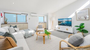 A modern living room with a sofa, a round wooden coffee table, a TV, and a large window.