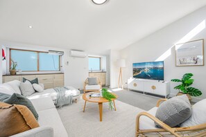 A modern living room with a sofa, a round wooden coffee table, a TV, and a large window.