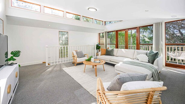 A spacious living area with a high ceiling, large windows, a white sofa, a wicker chair, and a small coffee table.