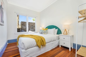 Une chambre à coucher avec un lit, une table de chevet, une fenêtre et un plancher en bois.