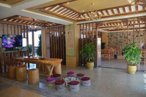 A traditional Japanese-style interior with tatami flooring, a wooden reception desk, a television, and potted plants. - Yingyue Lakeside Inn (Ninglang)