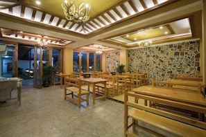 A restaurant with wooden tables and chairs, a stone wall, and a chandelier.