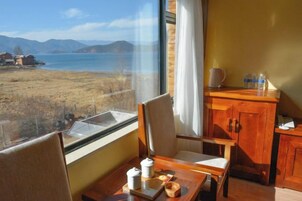A room with a view of a lake, a wooden cabinet, a table with a cup and saucer, and a chair.