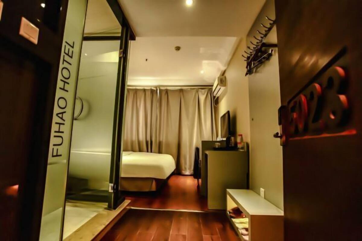 A hotel room with a bed, a desk, a mirror, and a door with the hotel name.