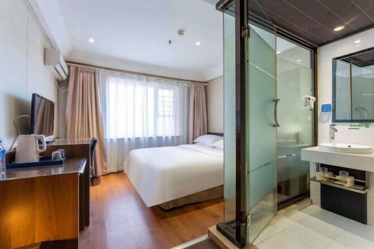 A hotel room with a bed, bedside table, and a glass-enclosed shower area.