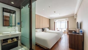 A hotel room with a modern design, featuring a large bed, a separate bathroom with a glass partition, and a small desk area. - Regal Hotel (Jiamusi Railway Station Department Store) (Jiamusi)