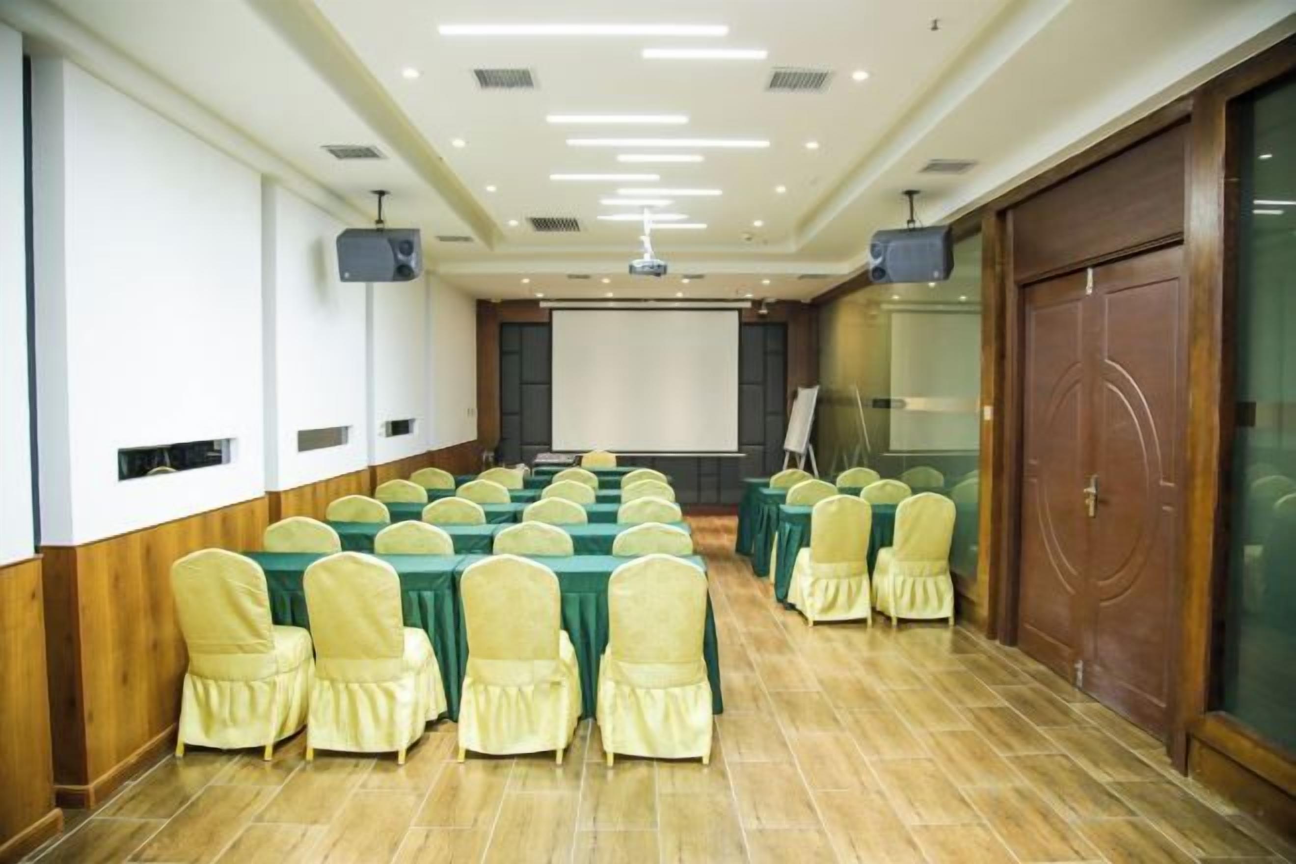 A conference room with rows of tables and chairs, a projector screen, and a presentation screen.