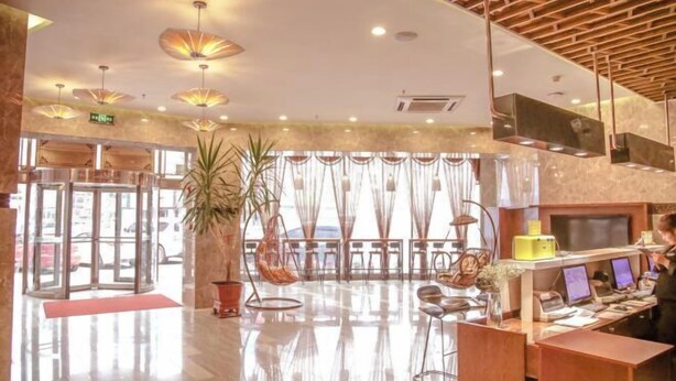 A hotel lobby with a revolving door, a reception desk with computers, and a large potted plant. - Regal Hotel (Jiamusi Railway Station Department Store) (Jiamusi)