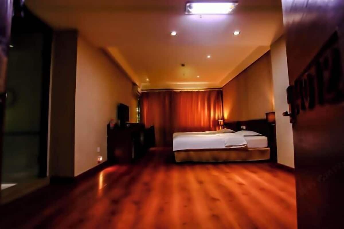 A hotel room with a wooden floor, a bed, a desk, and a window with curtains.