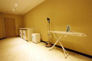 A laundry area with a washing machine, dryer, and ironing station. - Regal Hotel (Jiamusi Railway Station Department Store) (Jiamusi)
