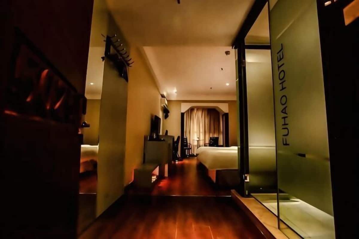 A hotel corridor with a bed, chairs, and a glass wall with the hotel name.