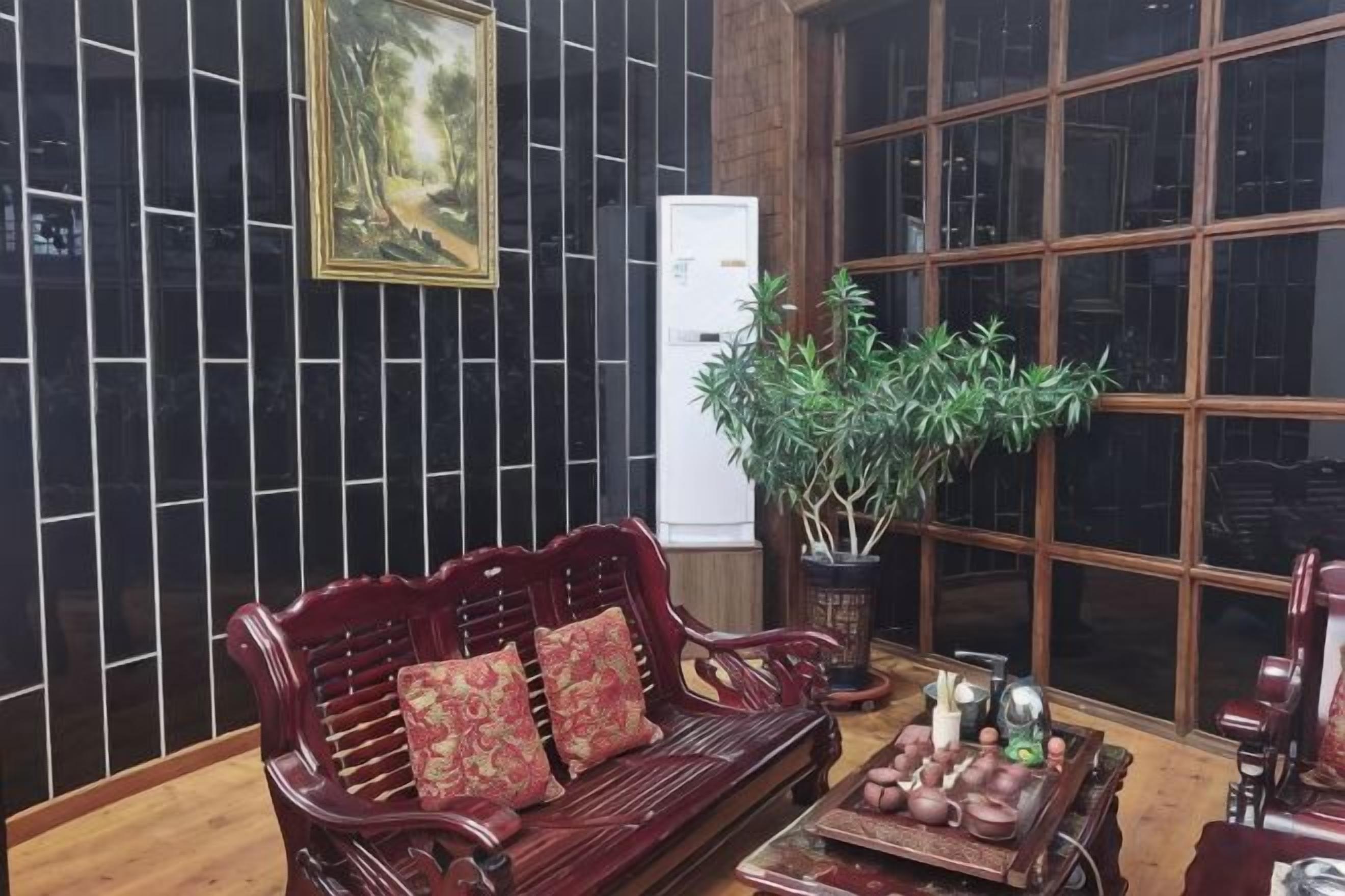 A room with a dark wooden wall, a large window, a wooden sofa with cushions, a table with decorative items, and a potted plant.