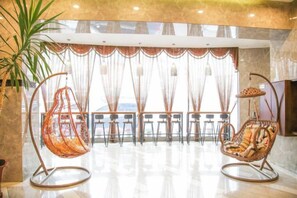 A lobby with two rocking chairs, a plant, and a view through a curtain. - Regal Hotel (Jiamusi Railway Station Department Store) (Jiamusi)