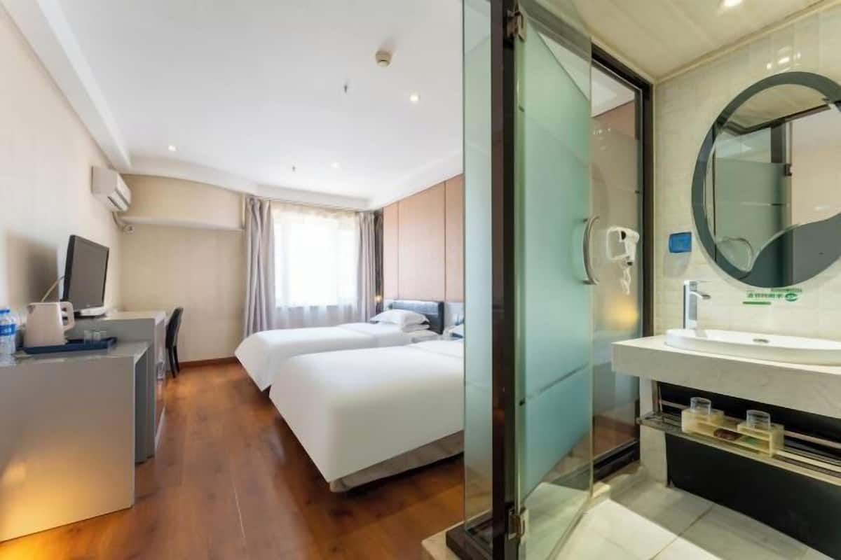 A hotel room with a desk, two beds, a large mirror, and a modern bathroom.