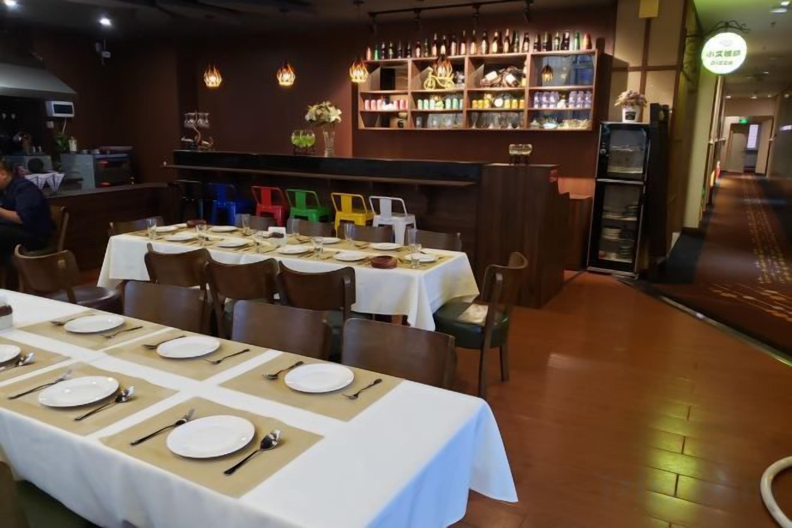 A restaurant with multiple tables set for dining, a bar area with shelves of bottles, and a counter.