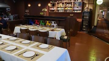 A restaurant with multiple tables set for dining, a bar area with shelves of bottles, and a counter.
