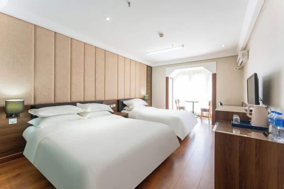 A hotel room with two beds, a desk with a flat-screen TV, a coffee maker, and a large window.