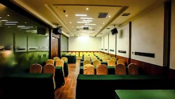 Un salón de conferencias con filas de mesas y sillas, una pantalla de proyector y una zona de escenario.