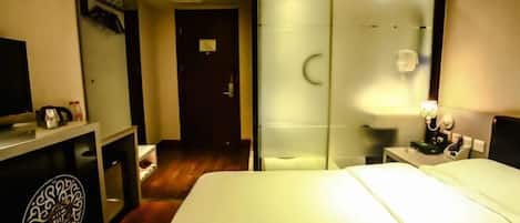A hotel room with a bed, a desk with a lamp, a mirror, and a wardrobe.